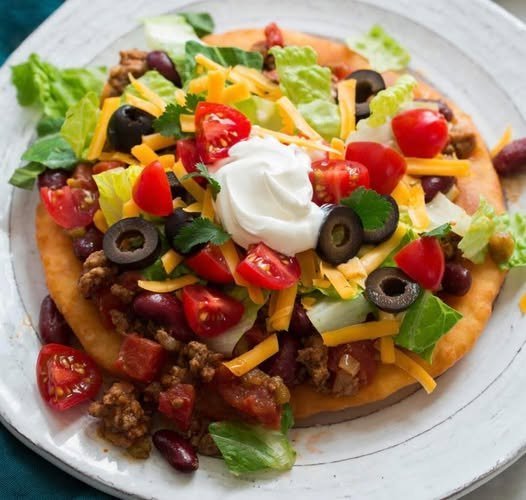 Navajo taco on golden fry bread topped with seasoned beef, beans, lettuce, cheddar, tomatoes, black olives and sour cream